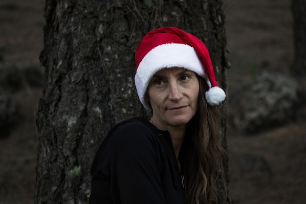 Portrait de femme sérieuse avec chapeau de Noël rouge par pin dans le parc forestier Dame pensive en hiver
