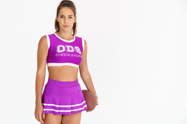 Portrait d'une femme sérieuse de pom-pom girl isolée sur un mur blanc tenant le handball pour le football américain.