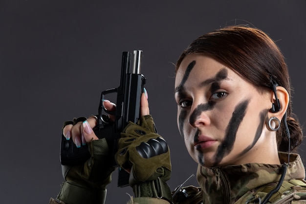 Portrait de femme soldat en uniforme militaire avec arme à feu sur le mur sombre