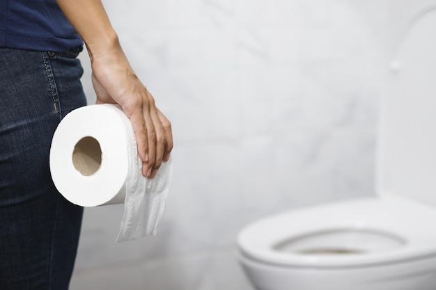 portrait d'une femme souffrant de diarrhée son estomac douloureux douleur et problème main tenir un rouleau de papier tissu devant la cuvette des toilettes constipation dans la salle de bain concept de soins de santé d'hygiène