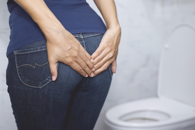 portrait d'une femme souffrant de diarrhée son estomac douloureux douleur et problème main tenir un rouleau de papier tissu devant la cuvette des toilettes constipation dans la salle de bain concept de soins de santé d'hygiène