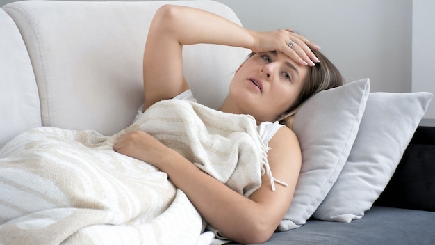 Portrait de femme souffrant de migraine allongée sur un canapé sous une couverture