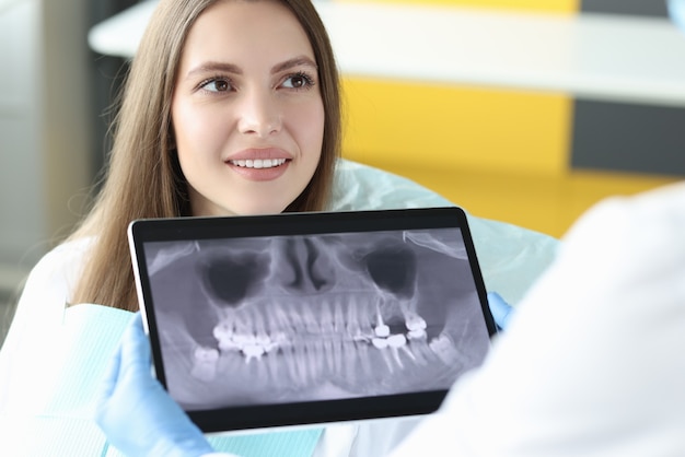 Portrait D'une Femme Souriante Au Rendez-vous Chez Le Dentiste Tenant Une Tablette Avec Une Image Radiographique De La Mâchoire