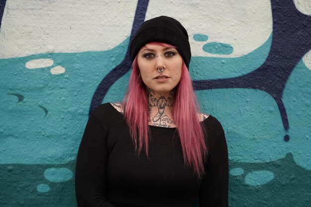 Photo portrait d'une femme souriante aux cheveux roses debout contre un mur de graffitis