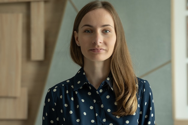 Portrait d'une femme souriante dans une chemise debout dans un bureau moderne