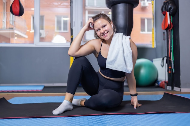 Portrait d'une femme souriante en forme de détente assise sur un tapis dans une pièce avec des fournitures de sport