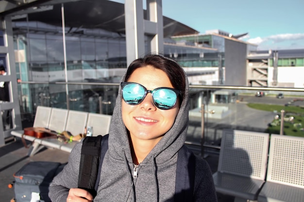 Photo portrait d'une femme souriante heureuse en lunettes de soleil avec sac à dos à l'aéroport