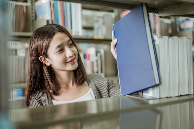 Portrait femme souriante heureusement ramassé un livre d'une étagère dans une bibliothèque universitaire. Concepts d'éducation, d'école, de bibliothèque et de connaissances.