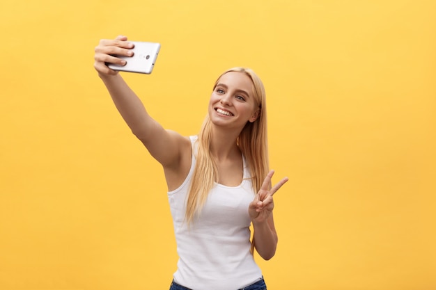 Portrait d&#39;une femme souriante joyeuse en chemise blanche prenant selfie isolé sur fond jaune