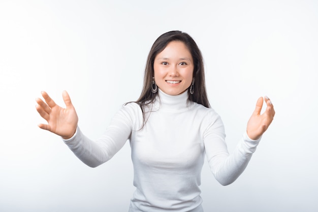 Portrait de femme souriante joyeuse faisant un geste de bienvenue sur le mur blanc