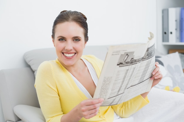 Portrait d&#39;une femme souriante, lisant un journal à la maison