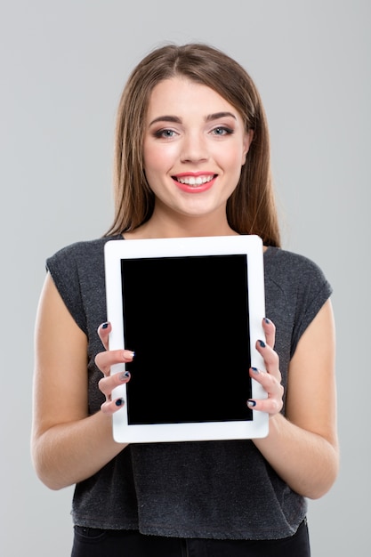 Portrait d'une femme souriante montrant un écran d'ordinateur tablette vierge isolé sur fond blanc