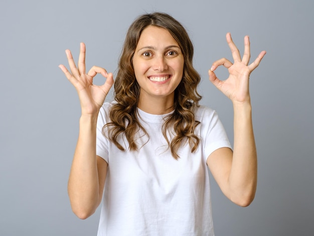 Portrait d'une femme souriante montrant un signe ok avec des doigts isolés sur un fond gris