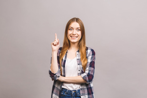 Portrait d'une femme souriante, pointant le doigt vers le haut à l'espace de copie isolé sur mur gris.