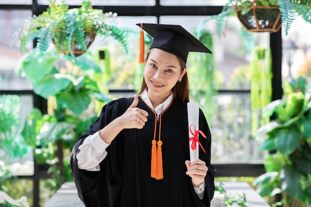 Portrait d'une femme souriante portant une robe de graduation debout contre la fenêtre