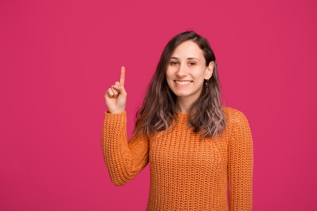 Portrait de femme souriante en pull pointant vers le haut au fond