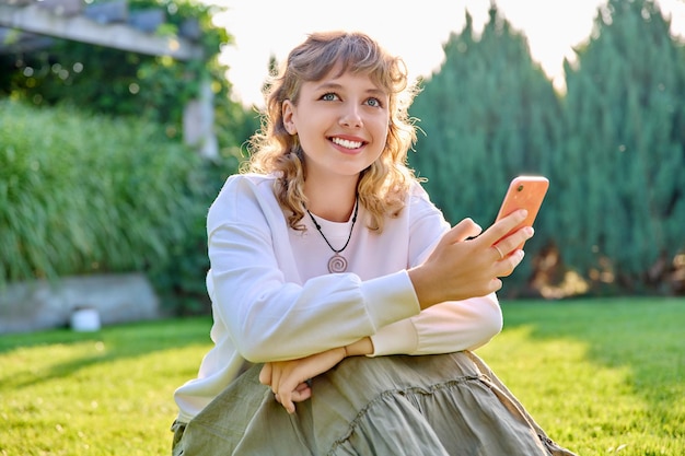 Portrait d'une femme souriante avec smartphone dans les mains assis sur l'herbe