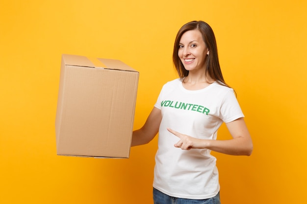 Portrait de femme souriante en t-shirt blanc avec inscription écrite titre vert volontaire avec grande boîte en carton isolée sur fond jaune. Aide d'assistance gratuite volontaire, concept de grâce de charité.