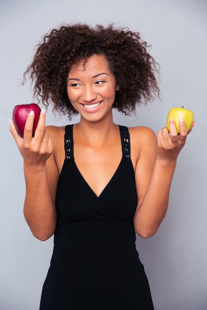 Portrait d'une femme souriante tenant des pommes sur un mur gris
