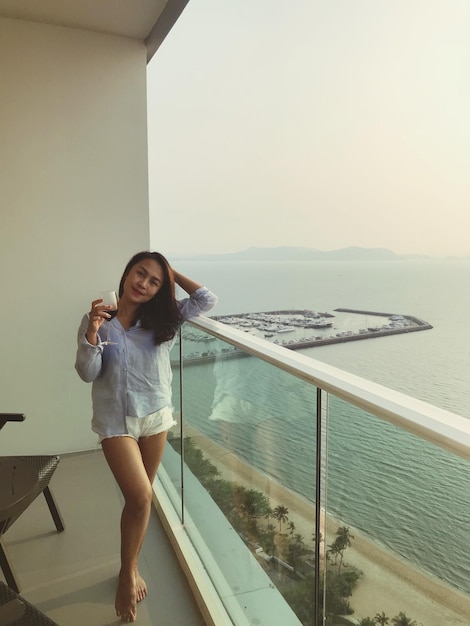 Photo portrait d'une femme souriante avec un verre de vin debout sur le balcon par la mer