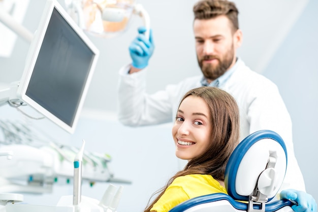 Portrait d'une femme avec un sourire à pleines dents assis au fauteuil dentaire avec un médecin en arrière-plan au cabinet dentaire