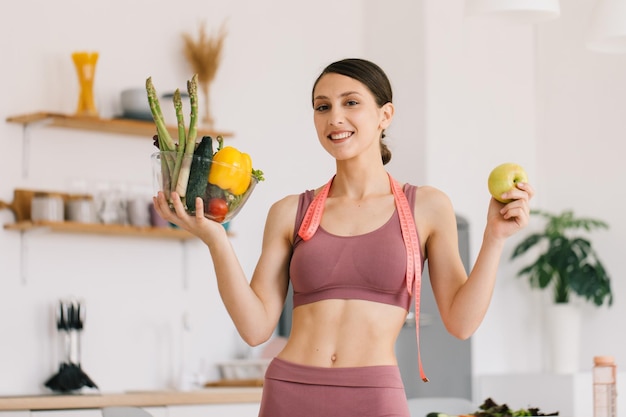 Portrait d'une femme sportive heureuse tenant une pomme et une assiette de légumes frais concept de saine alimentation