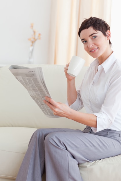 Portrait d&#39;une femme avec une tasse en lisant les nouvelles tout en regardant