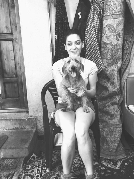 Photo portrait d'une femme tenant un chien assise sur une chaise.