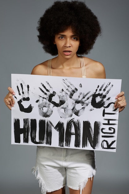 Portrait d'une femme tenant une pancarte avec du texte alors qu'elle se tient contre un fond gris