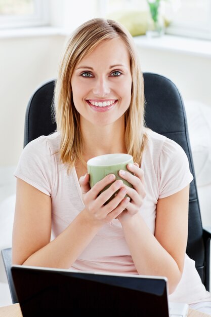 Portrait d&#39;une femme tenant une tasse de café et travaillant sur son ordinateur portable