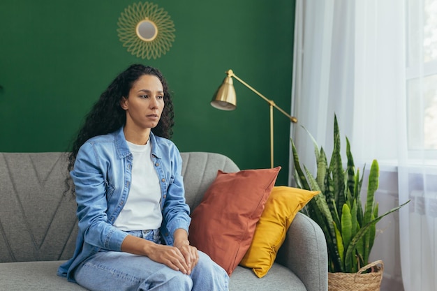 Portrait d'une femme triste seule à la maison pensive hispanic woman sitting on sofa in living room