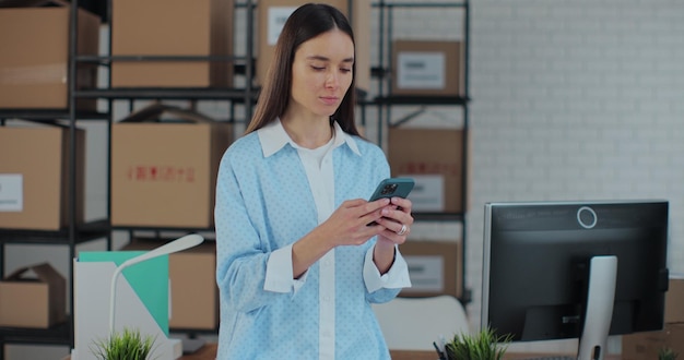 Portrait d'une femme utilisant un smartphone au travail dans un entrepôt Une femme se connecte au support client via Internet Responsable de travail dans une boutique en ligne