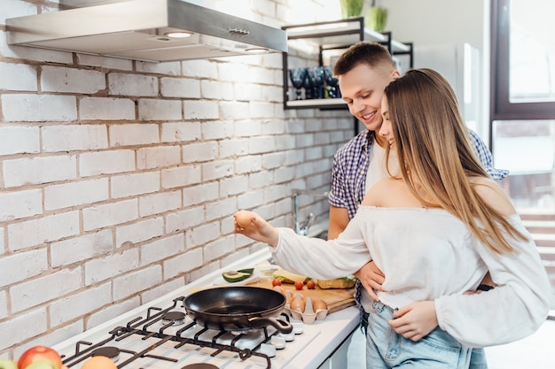 Portrait de femme va craquer un oeuf sur une poêle à frire sur le feu. Femme prépare le petit déjeuner avec un homme debout.