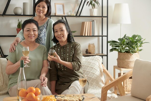 Portrait de femmes âgées gaies buvant du vin et mangeant des plats faits maison lors d'une fête à la maison