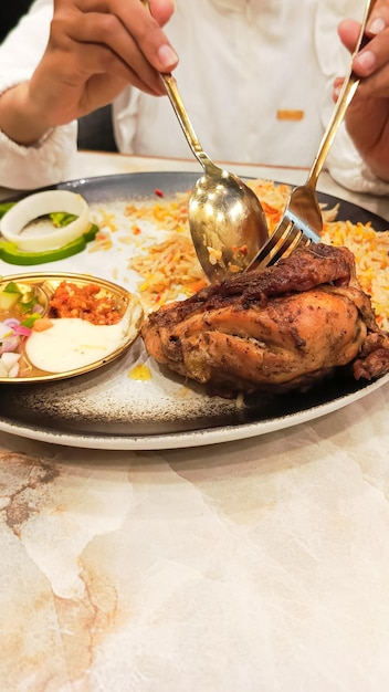 Photo portrait de femmes asiatiques à la main tranchant du poulet avec une cuillère et une fourchette sur une assiette de riz nasi kebuli