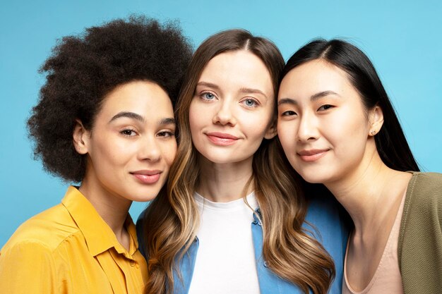 Portrait de femmes attrayantes de différentes ethnies souriantes ensemble sur un fond bleu