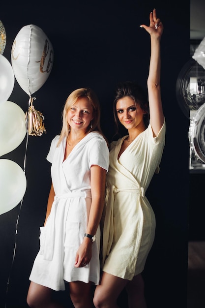 Portrait de femmes fortes et dangereuses avec maquillage posant à la caméra De superbes filles brunes levant les mains et dansant Des amis heureux se détendre à la fête près de ballons blancs et or