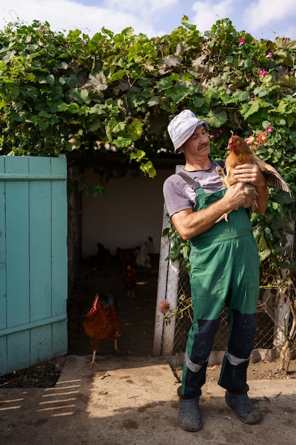 Portrait d'un fermier caucasien heureux tenant une poule brune en plein air Homme mûr souriant avec du poulet à la main avec espace de copie