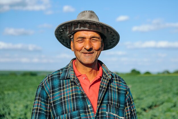 Le portrait d'un fermier en chemise à carreaux avec un chapeau sur la tête est satisfait du champ agricole Portrait en mouvement lent d'un vieux fermier regardant la caméra après une belle journée de travail