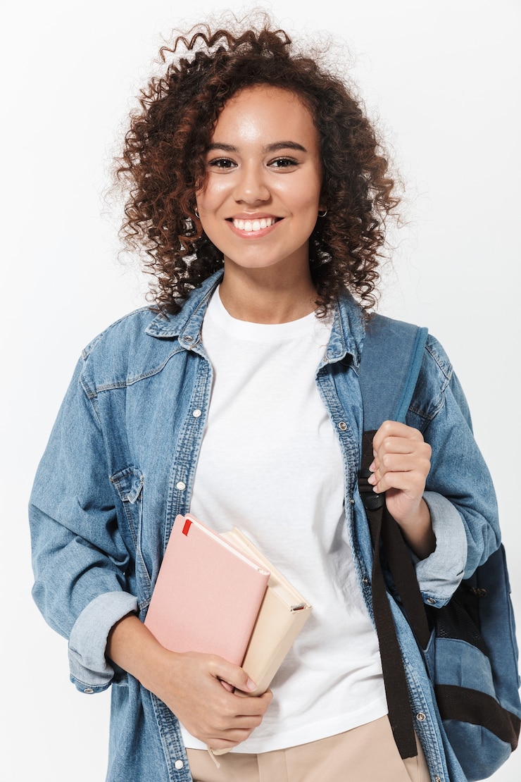 Photo portrait d'une fille africaine décontractée assez joyeuse portant un sac à dos debout isolé sur un mur blanc, tenant des manuels