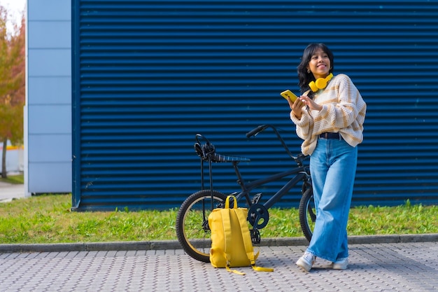 Portrait d'une fille asiatique écoutant de la musique avec un casque jaune sur un fond de collège bleu