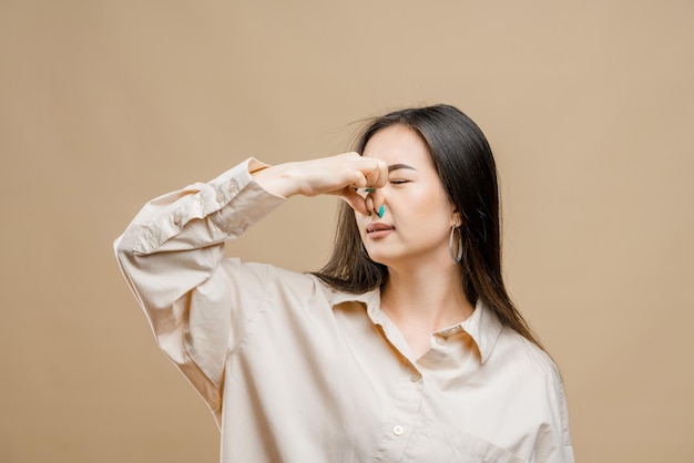 Portrait d'une fille asiatique sur fond marron clair Une fille asiatique a couvert son nez de l'odeur