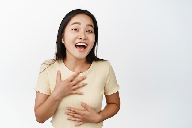 Portrait d'une fille asiatique heureuse riant et souriant regardant joyeusement la caméra debout en t-shirt sur fond blanc