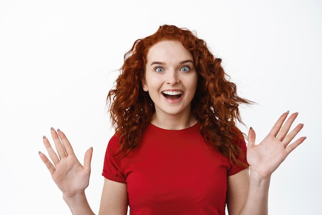 Portrait d'une fille au gingembre surprise aux cheveux bouclés, levez les mains et haletant, étonnée de vérifier une publicité impressionnante