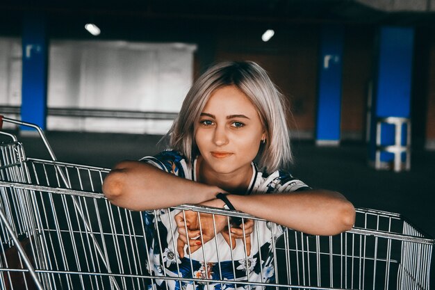 Portrait fille aux cheveux blancs courts vêtue d'un jean avec shopping grimpé dans le panier dans le parking