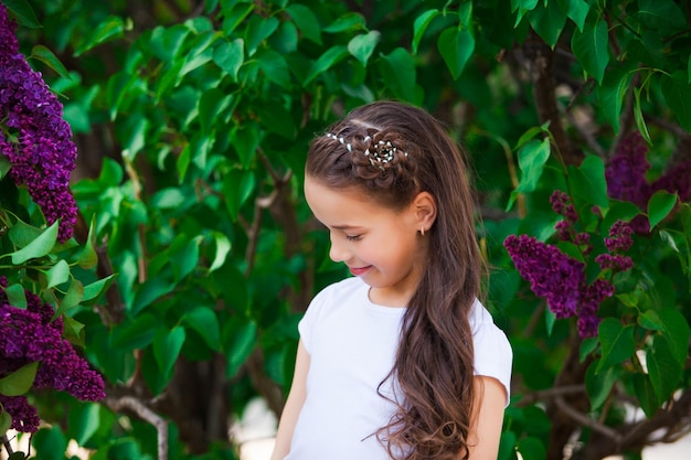 Portrait d'une fille avec une belle coiffure tressage de fleurs se tient parmi les feuilles vertes et le lilas violet