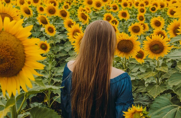 Portrait d'une fille belle, mignonne et sexy dans une robe bleue avec des fleurs de tournesol. Emotion de plaisir, concept de liberté, style de vie. Il se tient le dos aux cheveux longs.