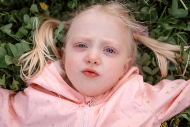 Photo portrait d'une fille blonde caucasienne aux yeux bleus allongée sur l'herbe verte petite fille towheaded à l'extérieur du printemps