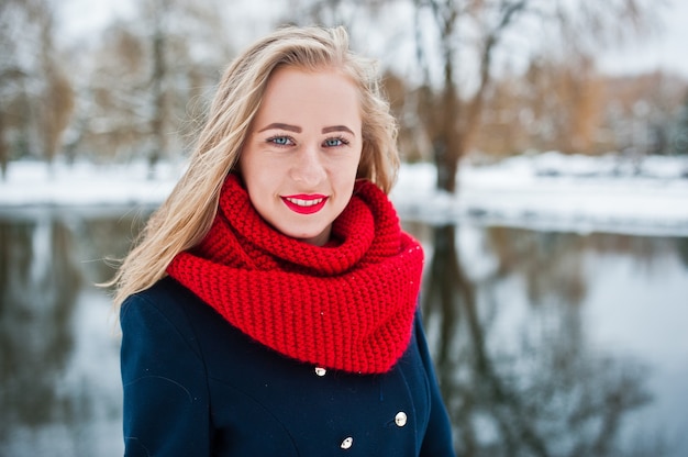 Portrait de fille blonde en écharpe rouge et manteau contre le lac gelé le jour de l'hiver.