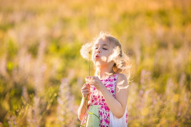 Le portrait d&#39;une fille blonde avec gros pissenlit dans le champ de fleurs au coucher du soleil.